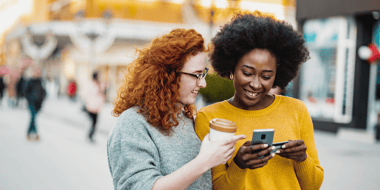 Two smiling women on the street holding a phone and credit card