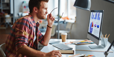 man sitting at desk looking at reports on computer