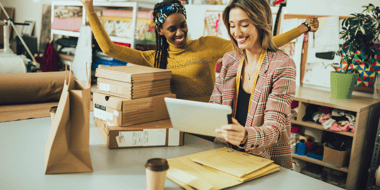 To ecommerce employees standing at desk with tablet celebrating